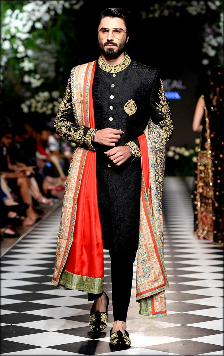 A groom wearing a black and gold sherwani with a maroon turban